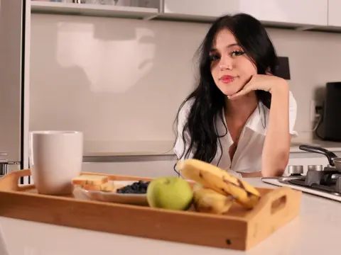 CuteBonniee — Young woman in a white shirt relaxing at a kitchen counter with a healthy breakfast tray of fruit.