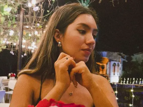 Young woman in a black strap top dining at a romantic outdoor restaurant with warm fairy lights at night.
