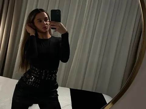 Young woman in a black long-sleeve top and leather skirt taking a moody mirror selfie in a bedroom.