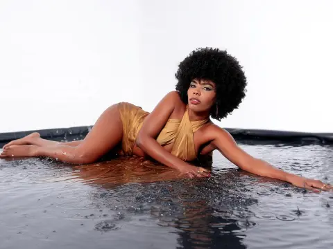 Elegant woman in a gold satin dress reclining in shallow water against a white background.