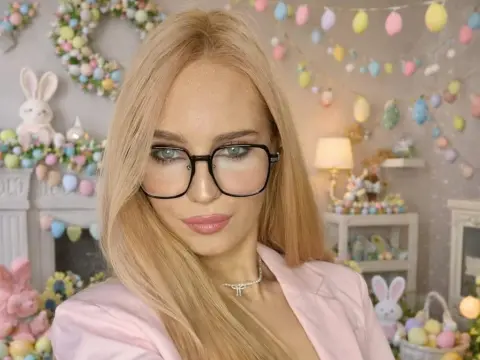 Blonde woman in pink outfit and black glasses posing in a festive pastel Easter decorated room.