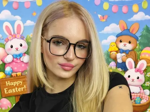 Blonde woman in black t-shirt and glasses smiling in front of a colorful cartoon Easter bunny backdrop.
