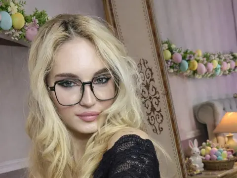 Blonde woman with black glasses wearing a black lace top in a bright room with pastel Easter decorations.