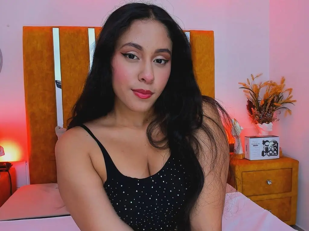 Marilyn_Hills — Marilyn_Hills poses in a black tank top with white polka dots against an orange headboard.