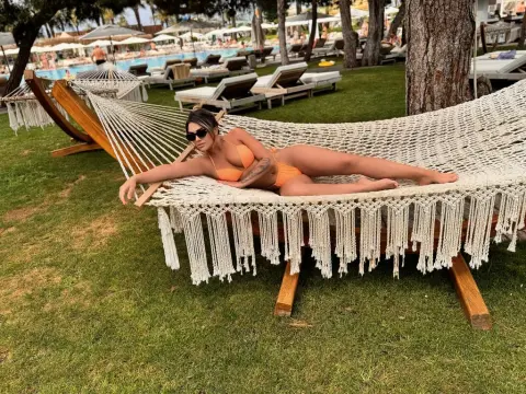 Relaxed woman in an orange bikini lounging on a white macrame hammock in a sunny tropical resort garden.