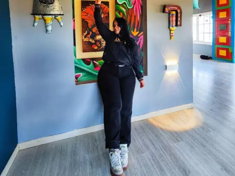 Cheerful woman in black streetwear and white sneakers posing in a colorful art gallery setting.