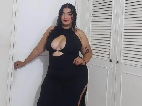 Curvy woman in a black cutout maxi dress posing confidently against a white door in a bright room.