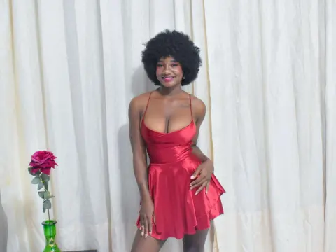 Smiling Black woman in a red satin mini dress posing against white curtains with a single rose.
