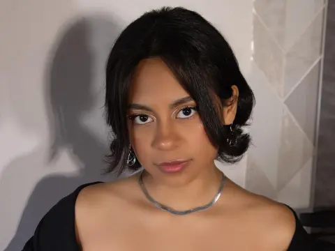 Young woman with dark hair and silver jewelry wearing a black top in a moody indoor setting.