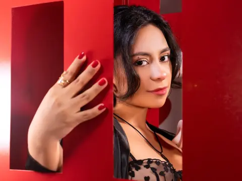 Young woman with dark hair in a black lace top peeking through red decorative panels with a moody expression.