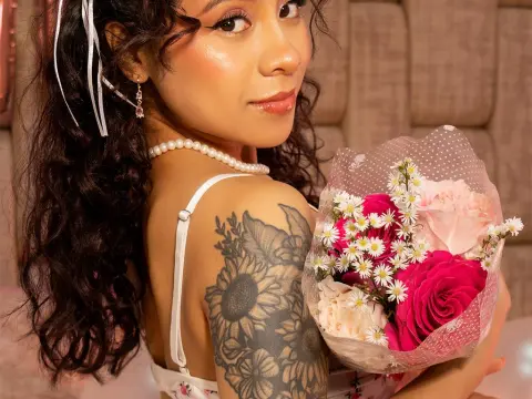 KarenMorgan — Young woman with curly hair and floral tattoo holding a pink rose bouquet in a cozy indoor setting.