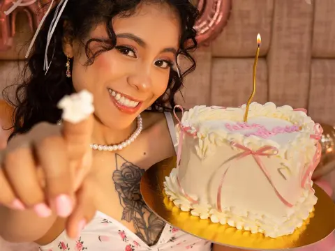 KarenMorgan — Smiling woman in a floral dress celebrating with a white frosted birthday cake in a festive pink setting.