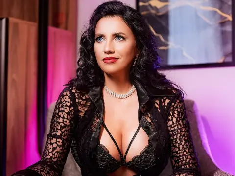 Elegant woman in black lace outfit and diamond necklace sitting in a moody, dimly lit room.