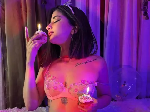 LaraJones — LaraJones wearing a pink lace bra and a tiara while eating a cupcake with a lit candle in purple lighting.