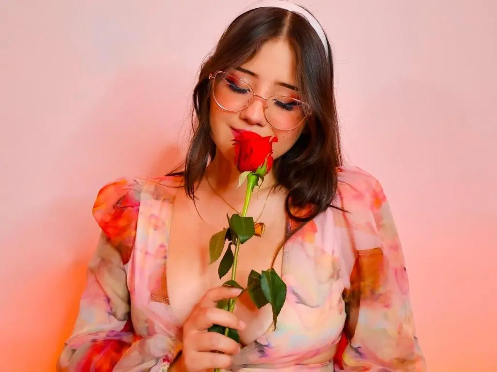 ImSophiaa222 — Dreamy portrait of a woman in a floral dress holding a red rose against a pink background.