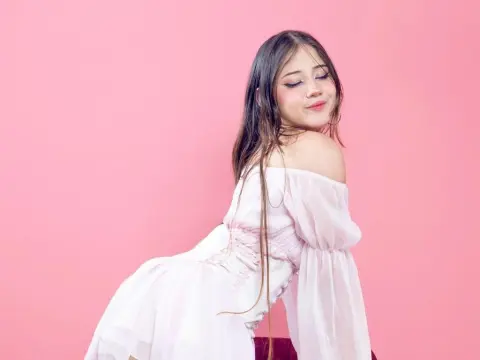 ImSophiaa222 — Young woman in a white off-the-shoulder dress posing against a soft pink background with a dreamy mood.
