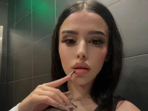 Young woman with long dark hair and glam makeup posing in a modern bathroom setting.