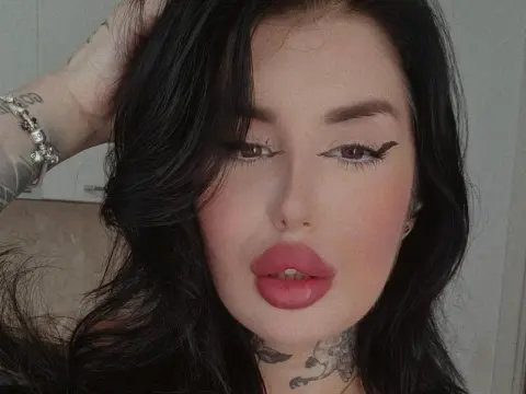 MallorieFoxx poses with long black hair and heavy winged eyeliner, showing off her full pink lips and neck tattoos.