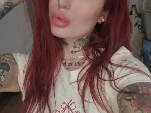 MallorieFoxx shows off her red hair and neck tattoos while wearing a white t-shirt in a close-up selfie.
