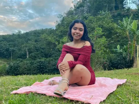 Julia_Bennett — Smiling young woman in a maroon dress sitting on a pink blanket in a lush green forest setting.