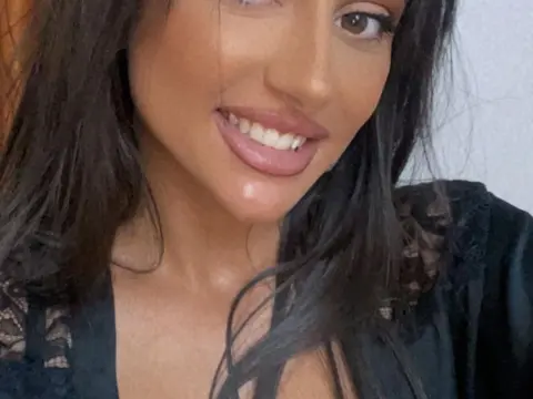 Dayana_Noir — Smiling young woman with long dark hair wearing a black lace outfit in a bright indoor setting.