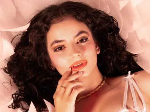 Beautiful woman with wavy dark hair and orange makeup relaxing in soft pink fabric.