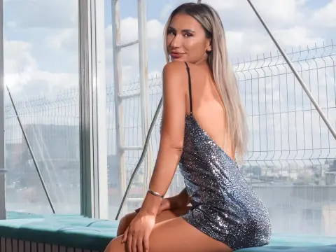 Glamorous woman in a silver sequin cocktail dress sitting by a bright window overlooking a city view.