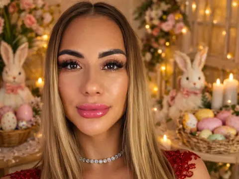 Smiling woman with long blonde hair and glamorous makeup in a festive Easter setting with bunnies and eggs.