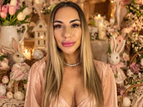 Smiling woman in a pink satin dress posing amidst pastel Easter bunnies and spring floral decorations.