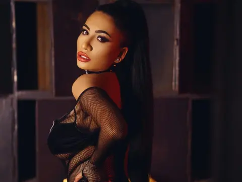 Glamorous woman in a black mesh outfit and choker posing with moody lighting in a dark indoor setting.