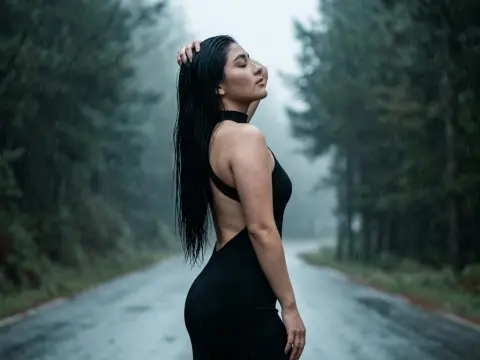Sophie_Winslow poses in a black backless dress with wet, long black hair against a misty forest road background.