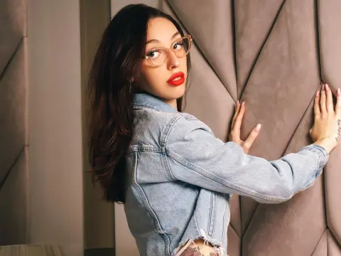 Stylish young woman in denim jacket and glasses posing against a tufted velvet wall with red lipstick.