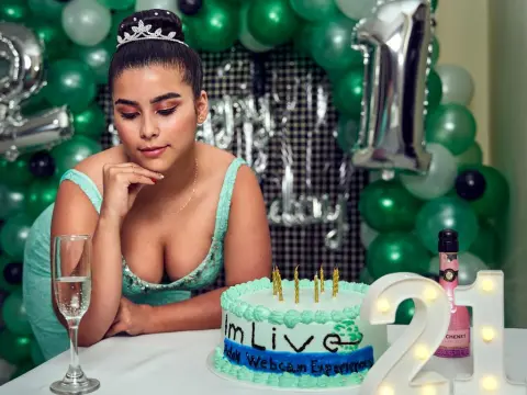Princes_Jasmine — Princes_Jasmine sits at a table with a birthday cake and champagne, wearing a low-cut teal dress and a silver tiara.