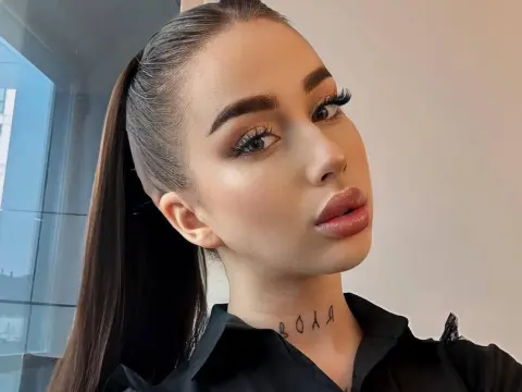 Glamorous woman with sleek high ponytail and heavy eye makeup wearing a black shirt in a bright indoor setting.