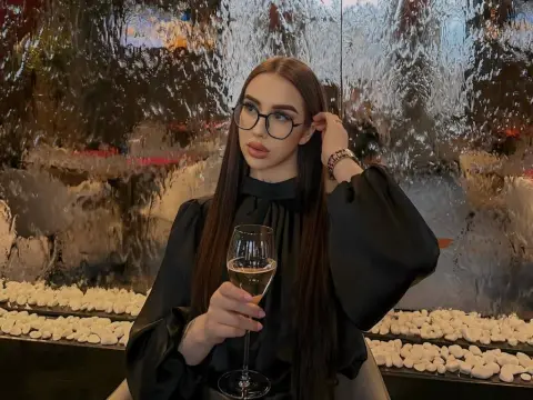 Elegant woman in a black blouse and glasses holding a glass of white wine by a shimmering water feature.