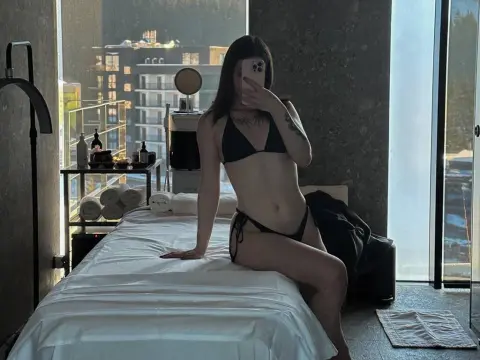 Young woman in a black bikini sitting on a massage table in a modern high-rise spa room with a city view.