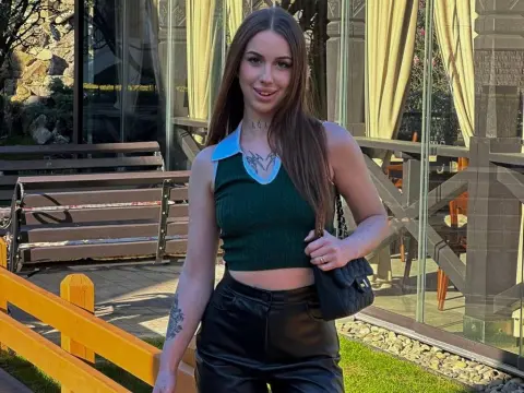 Young woman in a green ribbed tank top and black leather pants standing outdoors near a cafe patio.