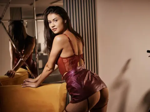 Young woman in red lace lingerie and burgundy leather skirt posing in a moody, modern indoor setting.
