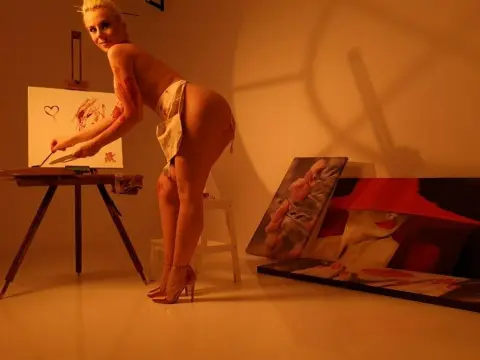 JennifferS — Nude blonde woman in a white wrap painting on canvas in a warm, moody art studio setting.