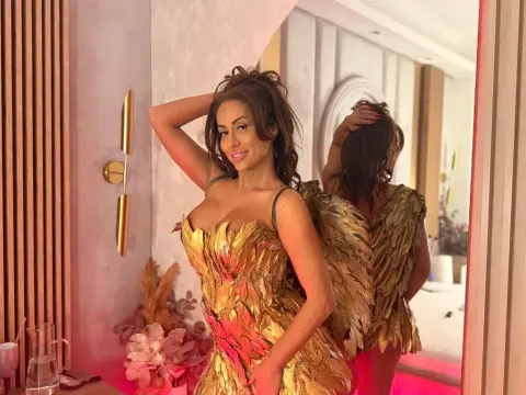Glamorous woman in a gold feathered gown posing in a modern, sunlit room with warm lighting.