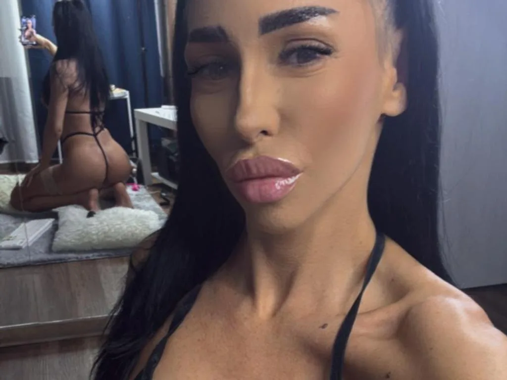 MyaBlakk — Young woman with long dark hair wearing black lingerie posing for a selfie in a bedroom setting.