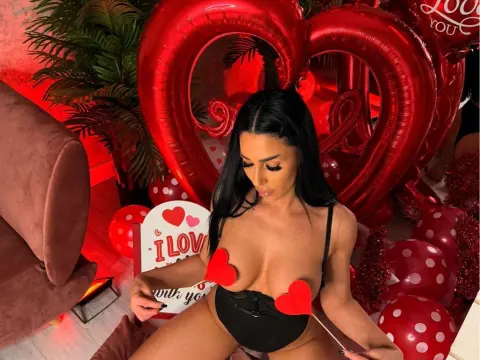 Brunette woman in black lingerie posing with red heart balloons in a romantic, festive setting.