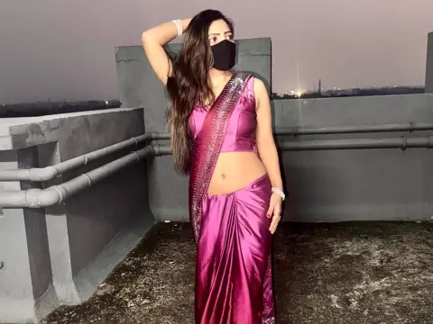 Woman in elegant pink satin saree posing on a rooftop at night wearing a black face mask.