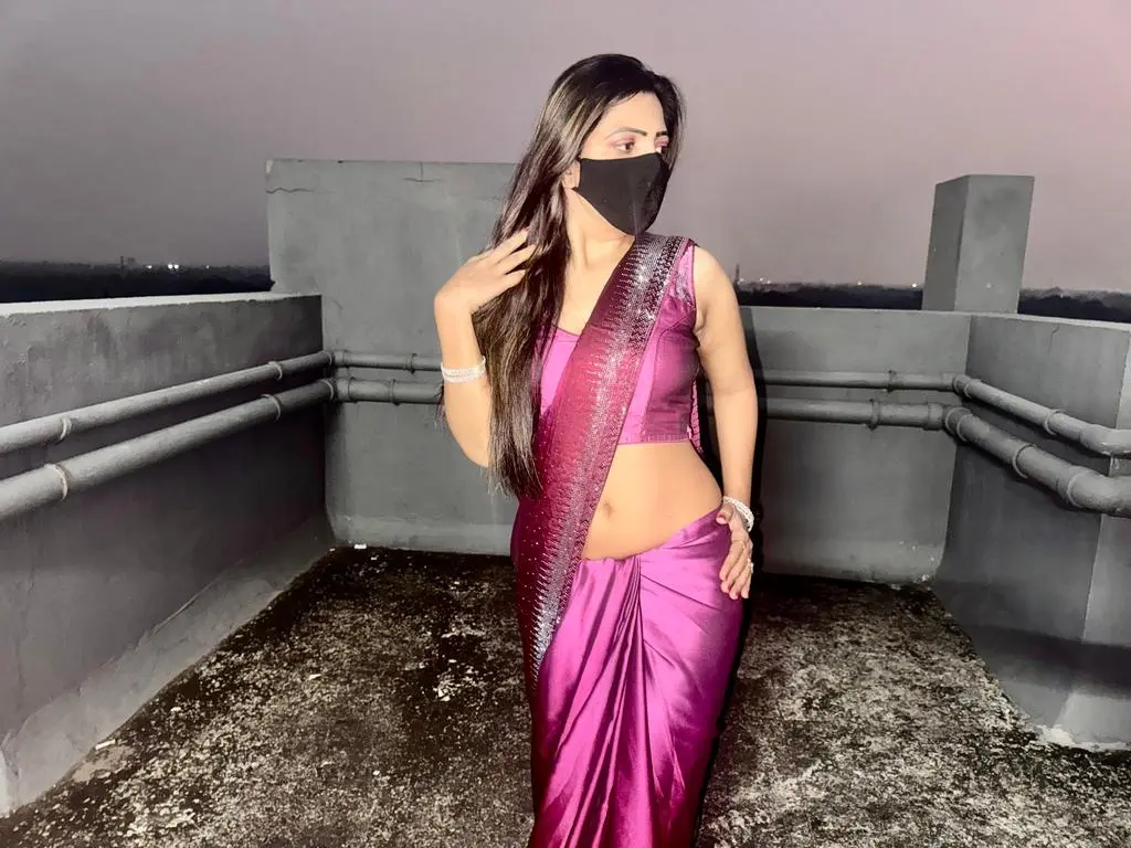 Elegant woman in a shimmering purple silk saree posing on a rooftop at night.