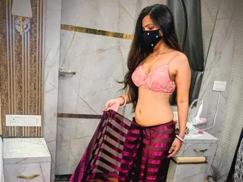 YoursPriya wears a pink lace bra and a purple striped sheer skirt, posing in a bathroom while wearing a black face mask.