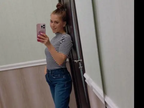 Young woman in a striped t-shirt and blue jeans taking a mirror selfie in a modern room.