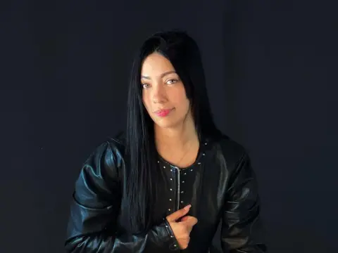 ashleesweett1 looks forward with long black hair while wearing a black leather jacket against a dark background.