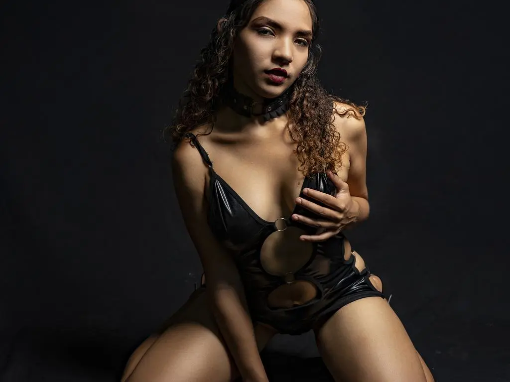 Young woman in black cutout bodysuit and choker posing against a dark moody background.