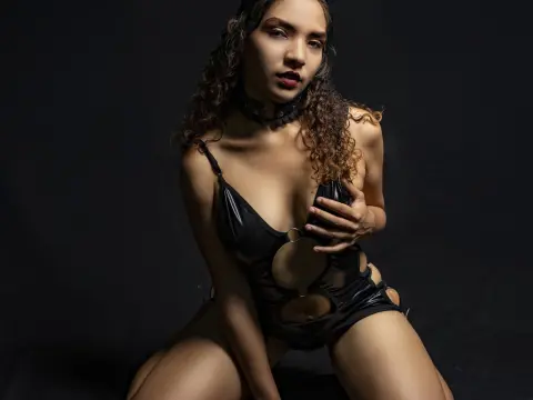 Glamorous woman in black leather bodysuit and choker posing against a dark moody background.