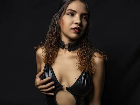 Young woman with curly hair in black leather outfit and choker posing against a dark moody background.